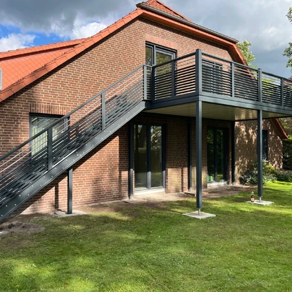 Modernes Backsteinhaus mit rotem Dach schwarzem Metalltreppenaufgang und Balkon