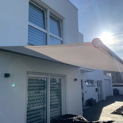 Weiße moderne Fassade mit Sonnensegel und großen Fenstern bei hellem Sonnenlicht